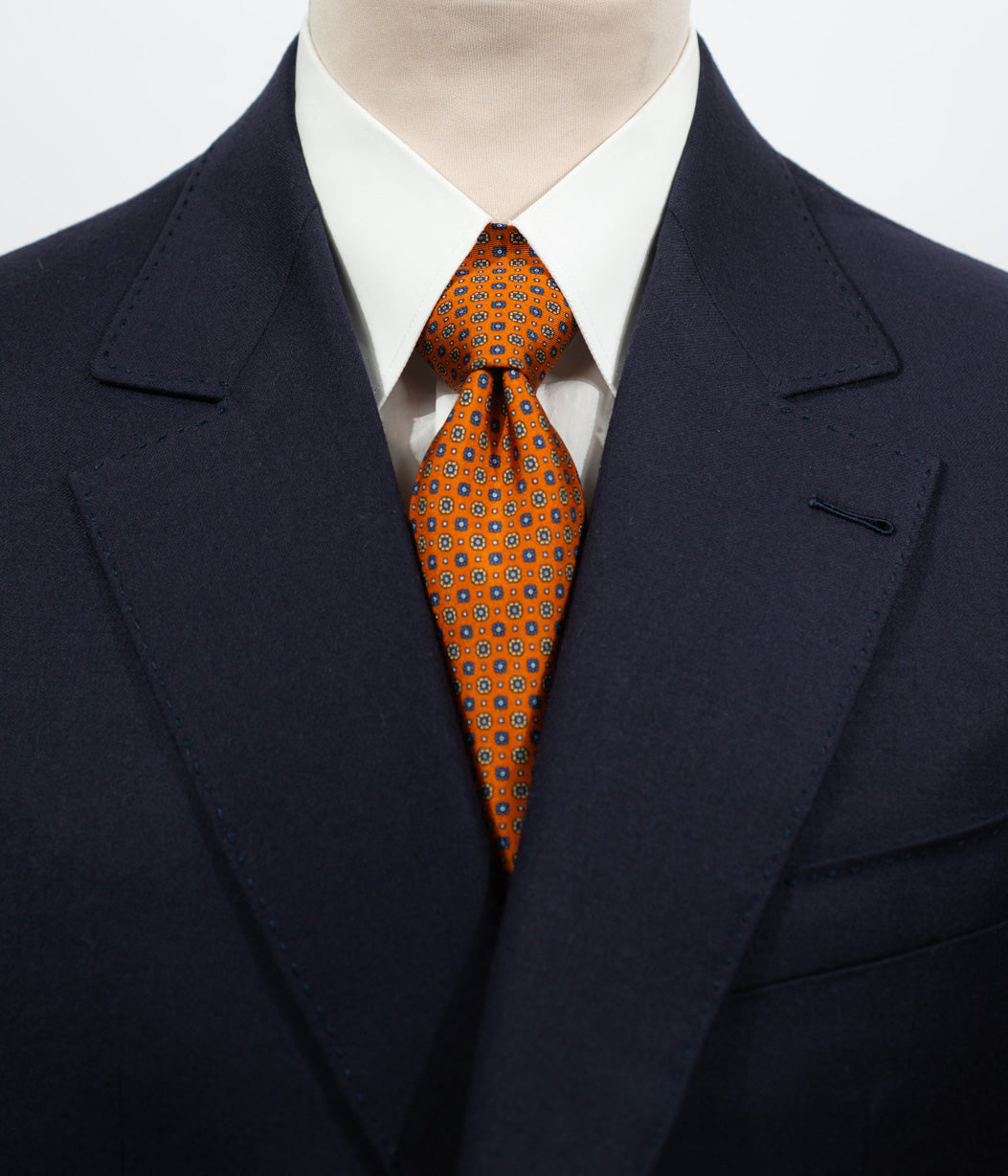 Cravate en twill 100% soie, ornée d'un motif de fleurs bleu et jaune sur fond orange